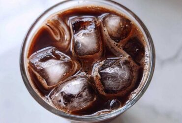 Overhead view of a glass filled with rich, dark chocolate milk and large ice cubes, perfect for iced chocolate milk.