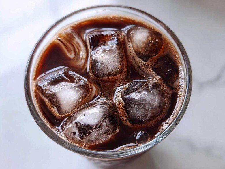 Overhead view of a glass filled with rich, dark chocolate milk and large ice cubes, perfect for iced chocolate milk.