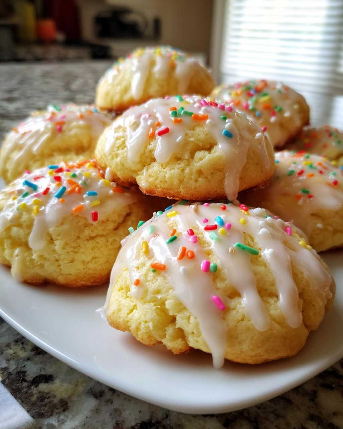 A stack of soft Italian ricotta cookies topped with white glaze and colorful sprinkles on a white plate.