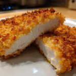 Close-up of juicy air fryer chicken breast cut in half showing white, cooked interior and crispy golden breading.