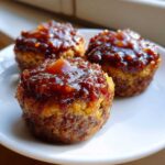 Close-up of three juicy mini meatloaf portions topped with a thick, shiny brown glaze on a white plate.