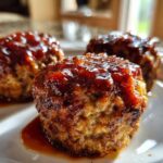 Three perfectly formed mini meatloaf portions topped with a thick, shiny glaze, resting on a white plate.