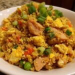 A close-up of a bowl of keto cauliflower fried rice mixed with scrambled egg, peas, carrots, and topped with green onions.