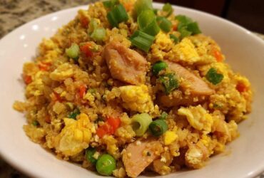 A close-up of a bowl of keto cauliflower fried rice mixed with scrambled egg, peas, carrots, and topped with green onions.