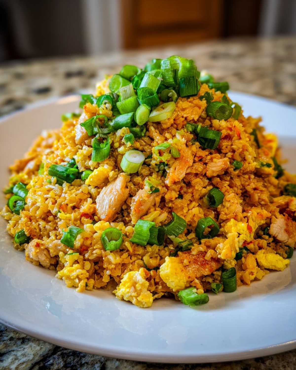 A mound of golden keto cauliflower fried rice mixed with chicken and egg, topped generously with fresh green onions.