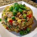 A mound of keto cauliflower fried rice mixed with egg, chicken, and vegetables, topped generously with fresh green onions.