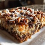 A single, thick slice of magic cookie bars topped with pecans, chocolate chips, and shredded coconut.