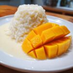 A serving of delicious mango sticky rice featuring bright yellow, cubed mango next to a mound of sweet sticky rice drizzled with coconut cream.