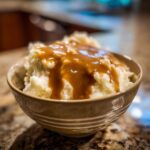 A close-up of creamy mashed potatoes generously topped with rich, brown chicken gravy in a small bowl.