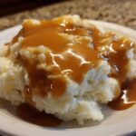 Close-up of fluffy mashed potatoes generously topped with smooth, brown chicken gravy on a white plate.