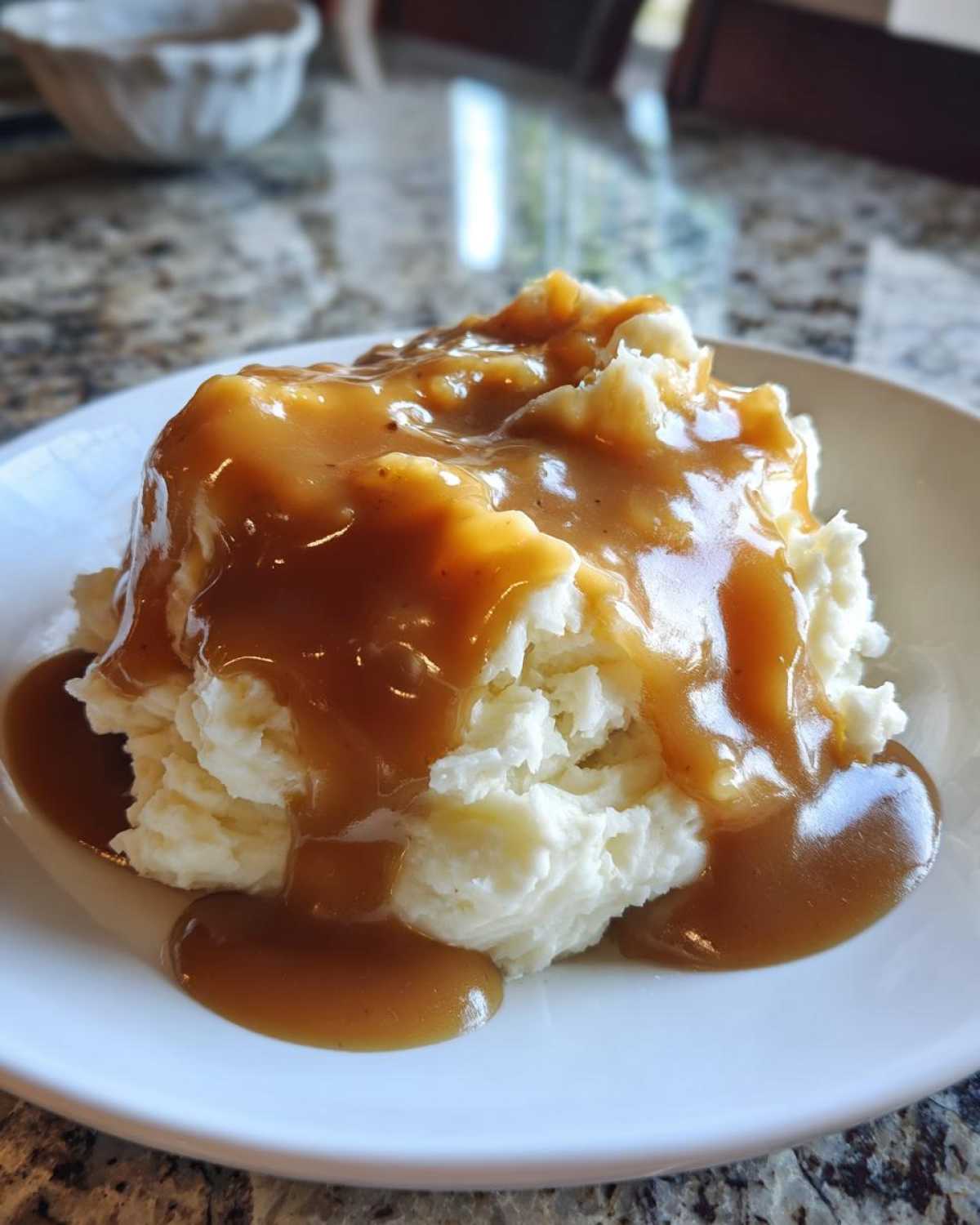 A serving of fluffy mashed potatoes generously topped with smooth, brown chicken gravy.