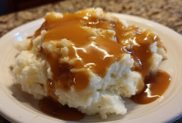 Close-up of fluffy mashed potatoes generously topped with smooth, brown chicken gravy on a white plate.