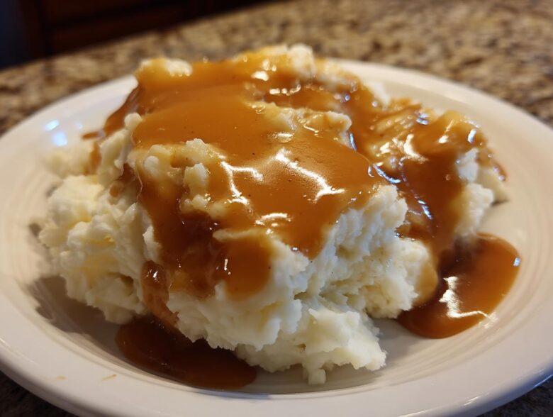 Close-up of fluffy mashed potatoes generously topped with smooth, brown chicken gravy on a white plate.