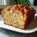 Close-up of a moist slice of homemade banana bread recipe with a golden crust on a white plate.