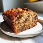 A close-up view of a slice of moist chocolate chip banana bread with a golden-brown crust.