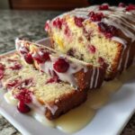 Two slices of moist cranberry orange bread drizzled with white glaze, served next to the loaf.