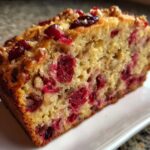 Close-up of a moist slice of cranberry walnut bread showing bright red cranberries and walnuts in the crumb.