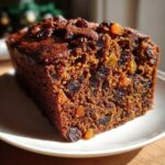 Close-up of a rich, dark, moist fruit cake recipe loaf, packed with raisins and dried fruit.