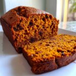Close-up of moist pumpkin bread loaf with a slice cut, showing a rich orange crumb and chocolate chips.