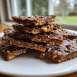 A stack of rich, dark chocolate Pecan Pie Bark pieces topped with chopped pecans, resting on a white plate.