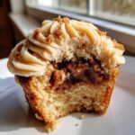 A close-up of a pecan pie cupcakes cut in half, showing the cake, pecan filling, and swirled frosting.