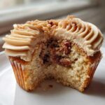 A close-up view of a pecan pie cupcakes cut in half, showing the cake interior filled with pecans and topped with brown sugar frosting.