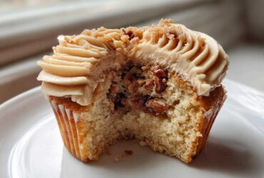 A close-up view of a pecan pie cupcakes cut in half, showing the cake interior filled with pecans and topped with brown sugar frosting.