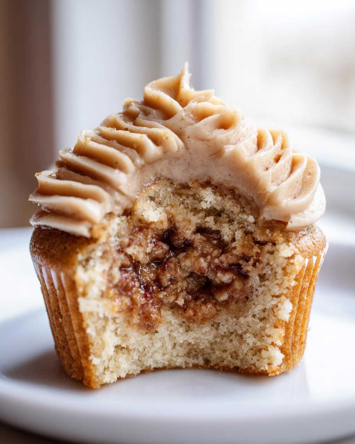 Close-up of a pecan pie cupcake cut in half showing the gooey filling and cinnamon frosting.