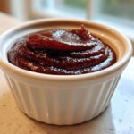 Close-up of thick, dark brown apple butter swirled high in a small white ramekin.
