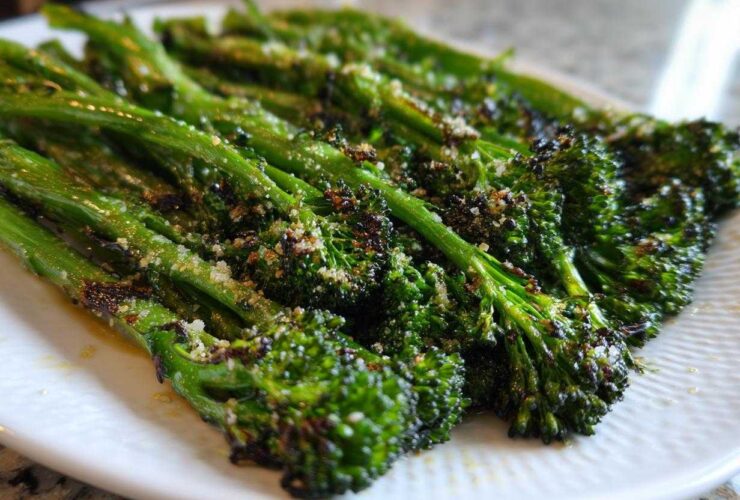 Close-up of roasted broccolini spears seasoned with grated cheese, highlighting the char marks.