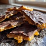 Close-up of broken pieces of homemade saltine cracker toffee topped with dark chocolate and gold sprinkles.