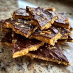 A stack of broken pieces of homemade saltine cracker toffee topped with melted chocolate and sea salt flakes.