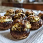 Close-up of freshly baked sausage stuffed mushrooms recipe arranged on a white platter.