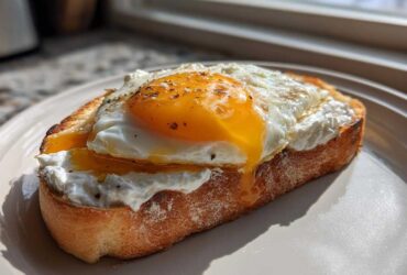A thick slice of toasted bread topped with creamy ricotta cheese and a runny sunny-side-up egg, seasoned with pepper. This is a savory ricotta toast.