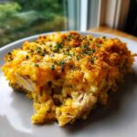 A close-up serving of creamy chicken wild rice casserole topped with melted orange cheese and parsley.