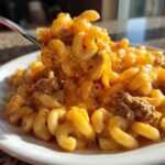 A fork lifts a generous portion of creamy, cheesy homemade hamburger helper mixed with ground beef from a white plate.