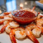 Plump, cooked shrimp arranged around a glass bowl of zesty red cocktail sauce for a classic shrimp cocktail presentation.