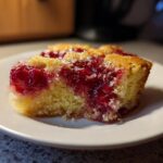 A close-up of a moist slice of cherry dump cake showing the bright red cherry topping and yellow cake base.