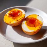 Two halves of soft-boiled marinated eggs showing gooey orange yolks, seasoned with dark spices.