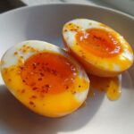 Two halves of soft-boiled marinated eggs showing jammy orange yolks, sprinkled with seasoning flakes.