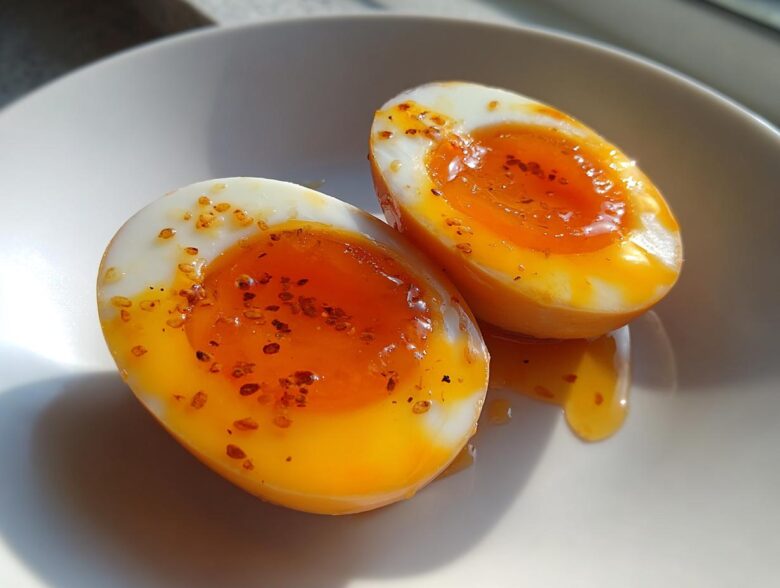 Two halves of soft-boiled marinated eggs showing jammy orange yolks, sprinkled with seasoning flakes.