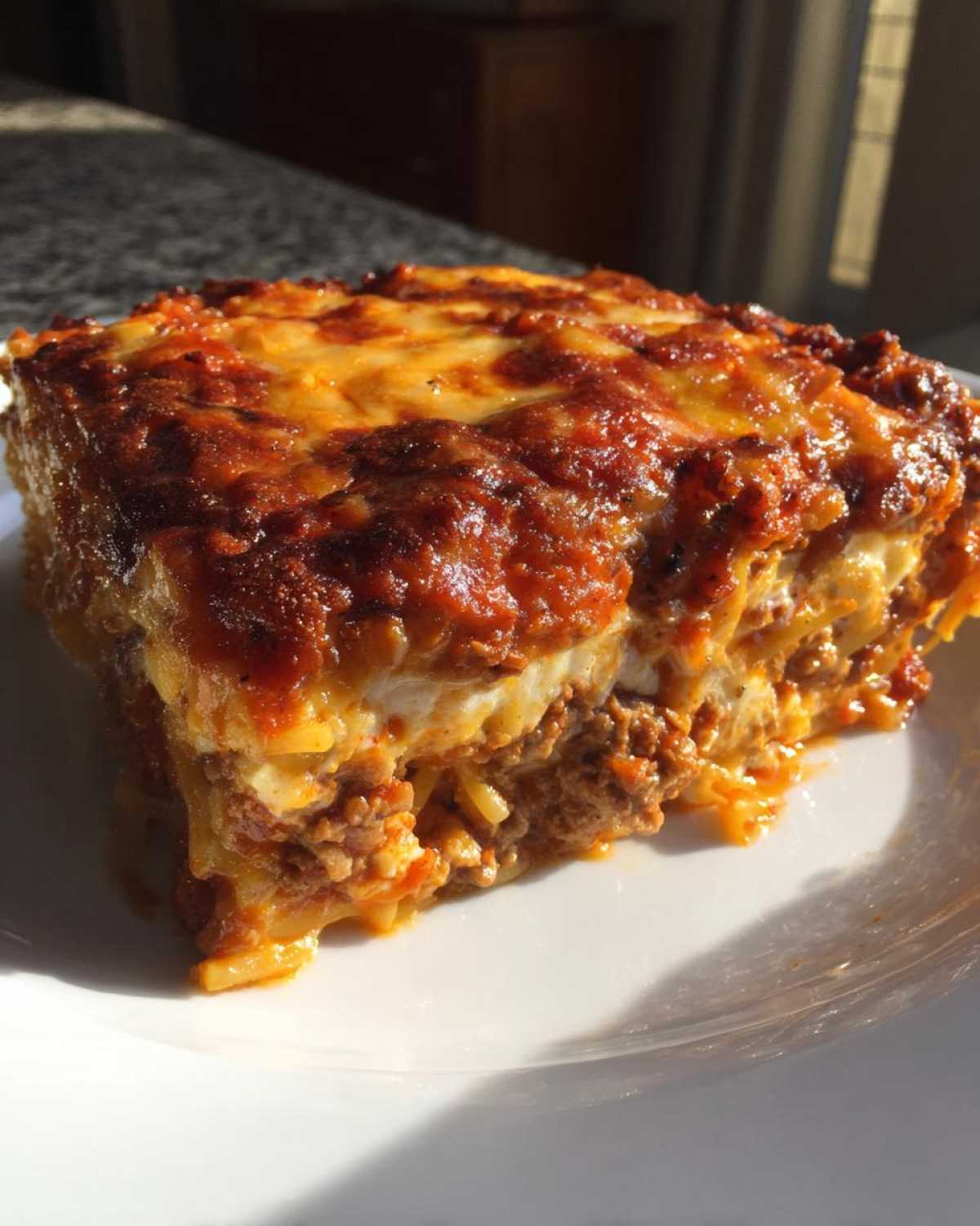 A close-up of a thick, square slice of baked spaghetti pie with layers of meat sauce and melted cheese.