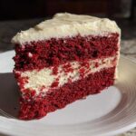 A perfect slice of red velvet cheesecake with deep red layers and creamy white filling, served on a white plate.