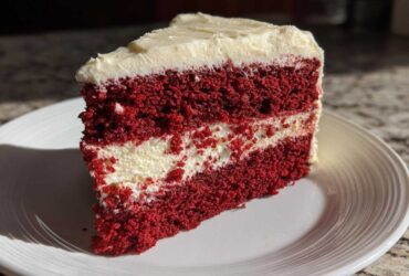 A perfect slice of red velvet cheesecake with deep red layers and creamy white filling, served on a white plate.