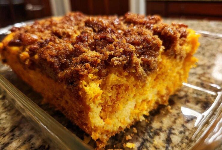 A close-up view of a square serving of bright orange sweet potato souffle topped with a dark brown, sugary crumb topping.