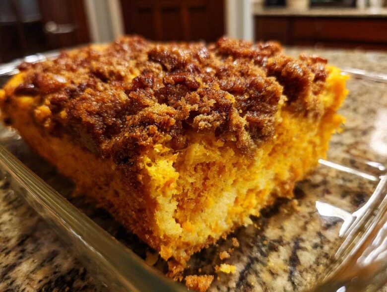 A close-up view of a square serving of bright orange sweet potato souffle topped with a dark brown, sugary crumb topping.