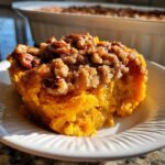 A close-up serving of bright orange sweet potato souffle topped with crunchy brown sugar and pecan streusel.