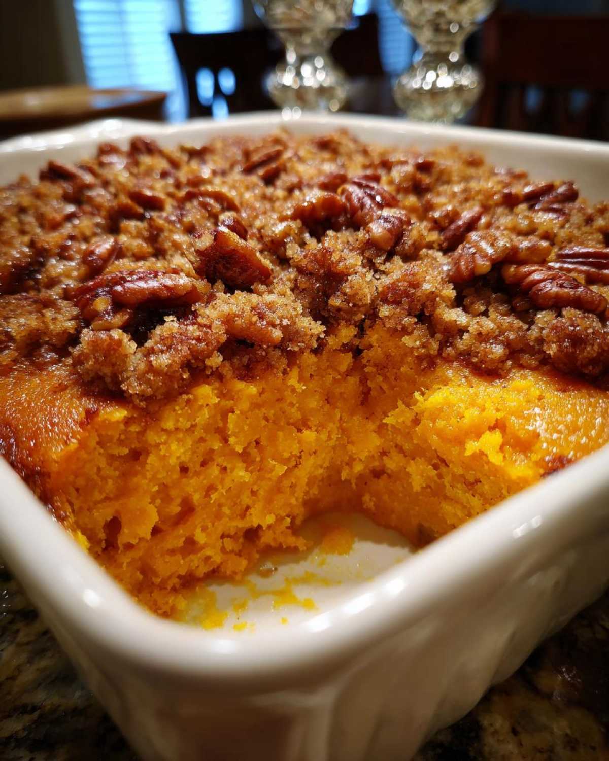 A scoop has been taken out of a bright orange sweet potato souffle topped with brown sugar and pecans.