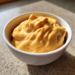 Close-up of thick, vibrant orange nacho cheese sauce served in a small white bowl.