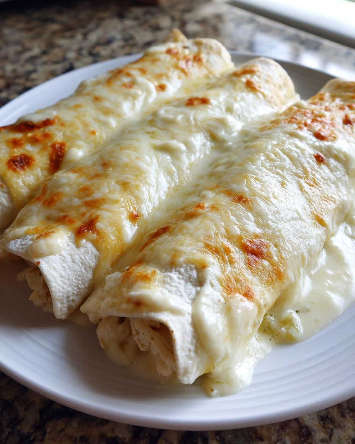 Three rolled white chicken enchiladas smothered in melted, slightly browned white cheese sauce.